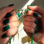 Green onyx drop charm, molten skull charm, small emerald charm lock, on a green faceted opal necklace in hand.