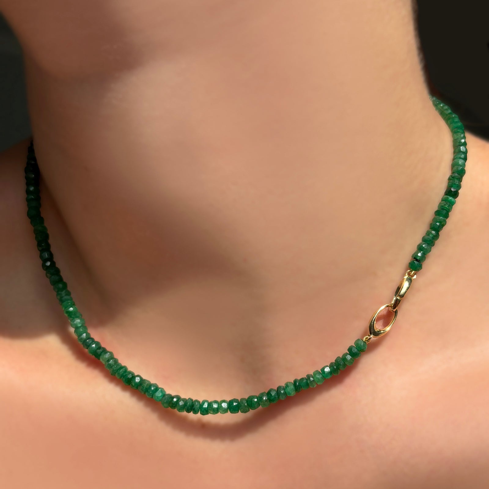 Green faceted emerald necklace with the 14k yellow gold linking ovals clasp towards the front on a model's neck.