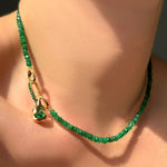 Green faceted emerald necklace with an emerald charm lock and molten knot charm with rose cut emerald on a model's neck.