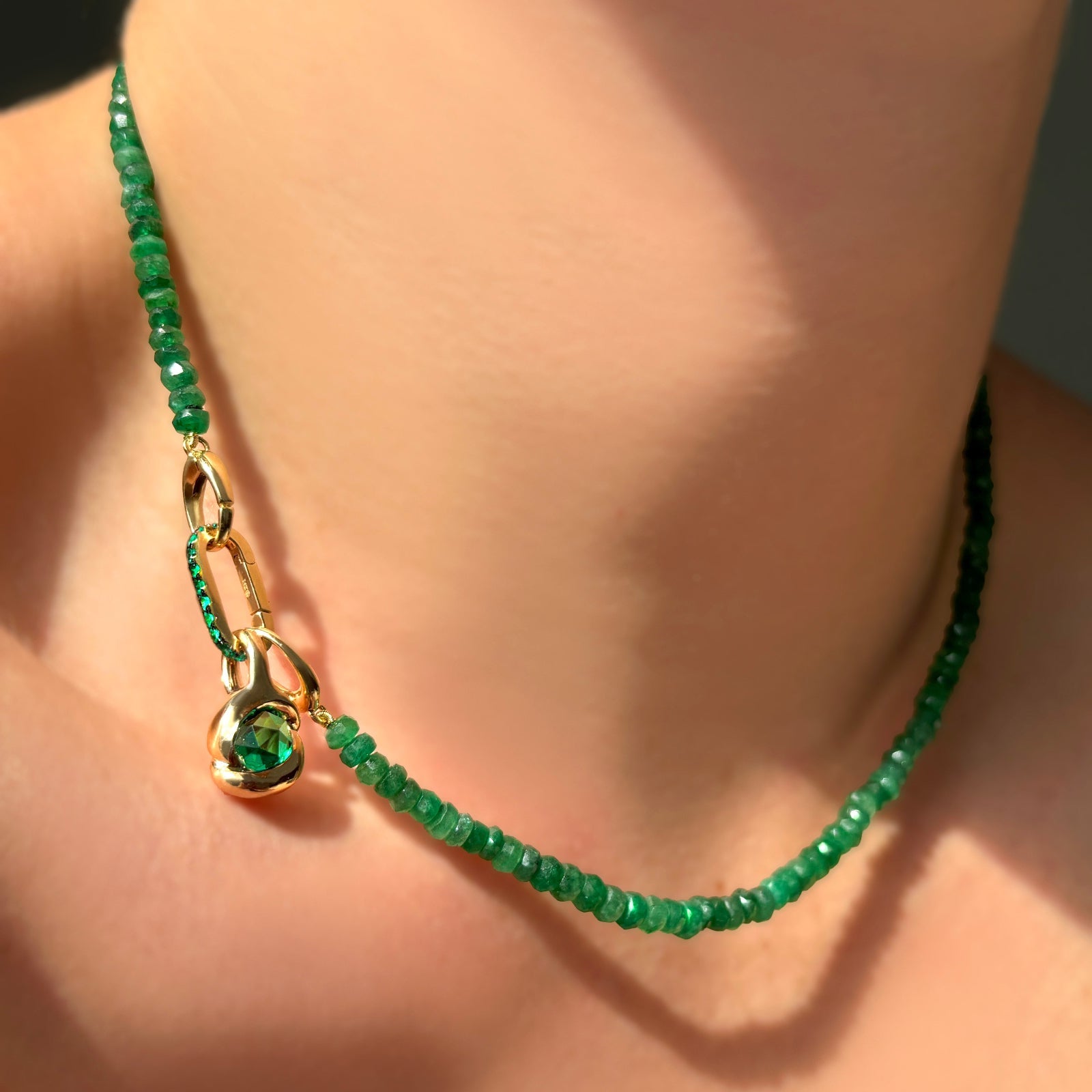 Green faceted emerald necklace with an emerald charm lock and molten knot charm with rose cut emerald on a model's neck.