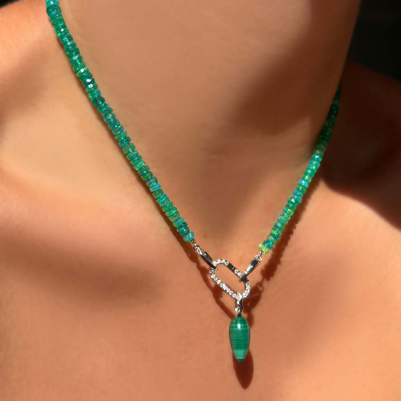 A model wears a a green grass faceted opal necklace, with a pavé face charm lock, and a malachite drop charm.