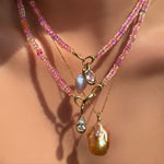 AMANDA PEARL Hibiscus Sapphire Necklace with blue lace agate drop charm and molten knot charm with amethyst layered over another sapphire necklace with molten solitaire charm with pear shaped diamond, over a diamond cut bead chain with blush baroque pearl charm on a model's neck.
