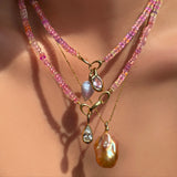 AMANDA PEARL Hibiscus Sapphire Necklace with blue lace agate drop charm and molten knot charm with amethyst layered over another sapphire necklace with molten solitaire charm with pear shaped diamond, over a diamond cut bead chain with blush baroque pearl charm on a model's neck.