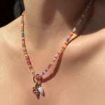High-biscus opal necklace with beaded round charm lock, molten knot charm with amethyst, and blue lace agate drop charm hanging from the neck.