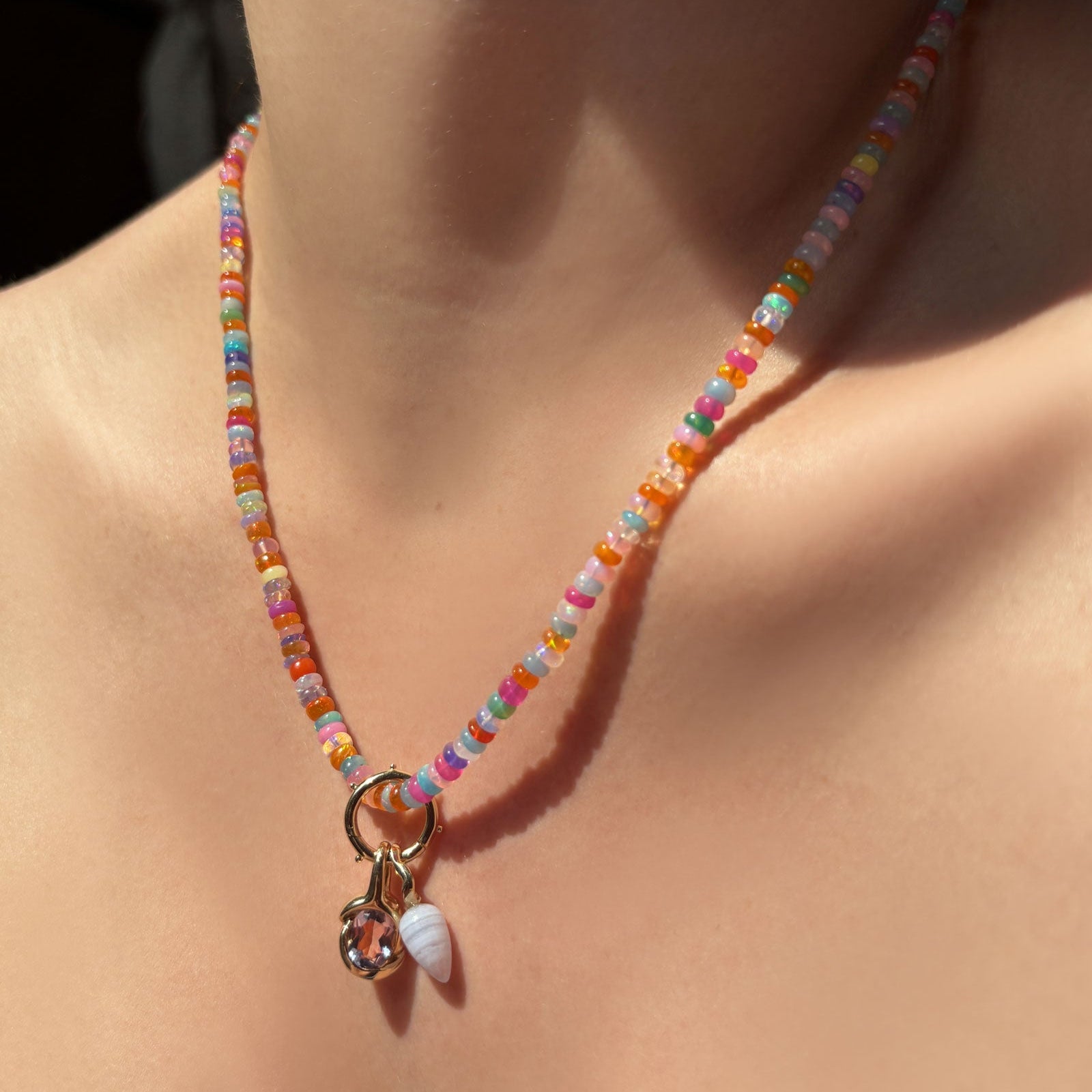 High-biscus opal necklace with beaded round charm lock, molten knot charm with amethyst, and blue lace agate drop charm hanging from the neck.