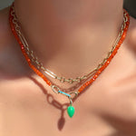 Irregular cable chain layered with a faceted carnelian necklace with turquoise charm lock holding a chrysoprase drop charm on a model's neck.