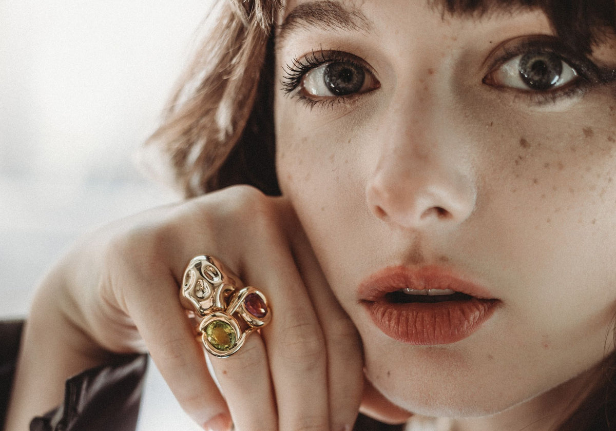 Brunette with a stack of molten rings on one finger including molten skull ring and two colorful molten knot rings.