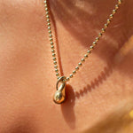 14k recycled Gold Molten Drop Charm styled on a gold bead chain on a neck.