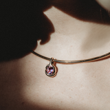 Molten knot charm with amethyst gemstone. Styled on a model's neck hanging from a yellow gold omega chocker necklace.