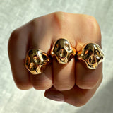 Three 14k recycled gold skull rings on three fingers in the shape of a fist