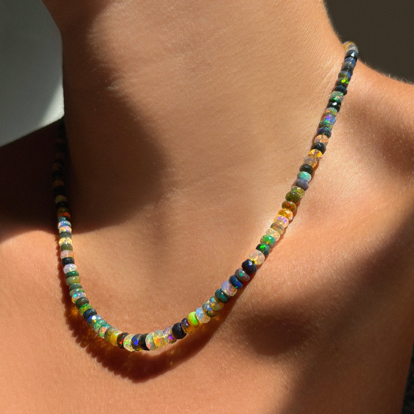 Shimmering beaded necklace made of faceted opals in shades of green, blue, purple, and white on a gold linking ovals clasp styled on a neck