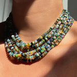 Shimmering beaded necklace made of faceted opals in shades of green, blue, purple, and white on a gold linking ovals clasp styled on a neck styled with multiple stands