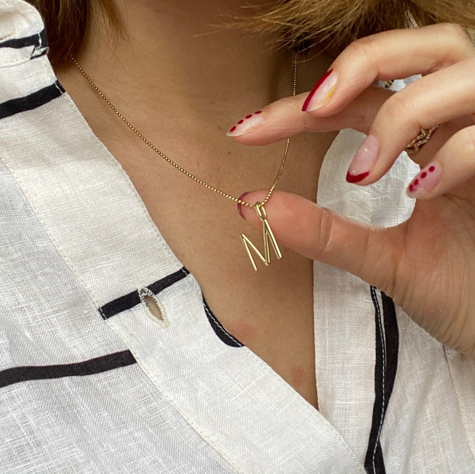 A model shows off her M letter charm in 14K recycled yellow gold, lifting it with a manicured hand. 