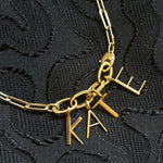 14K recycled yellow gold letter charms spell out the name "KATE" attached to small oval charm locks and a paperclip chain. 