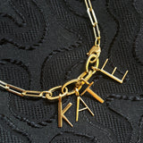 14K recycled yellow gold letter charms spell out the name "KATE" attached to small oval charm locks and a paperclip chain. 