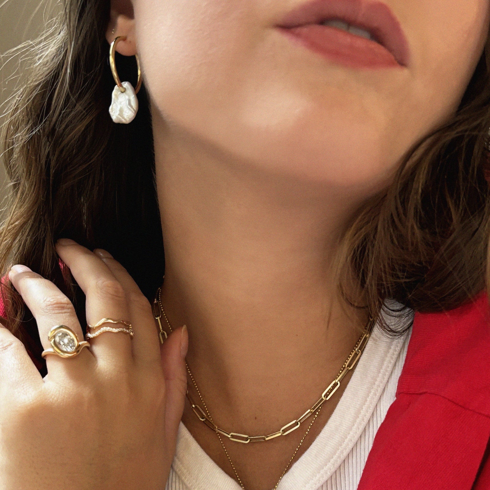 Megan wearing the Molten Knot Ring with Diamond in yellow gold, wide ripple ring in yellow gold, and ripple ring - full pave in yellow gold on her hand. Pearl hoop earring worn on one of the ears.