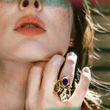 Molten knot ring with deep, rich purple amethyst gemstone layered with a molten knot ring with green tourmaline and a molten skull ring on a model's hand.