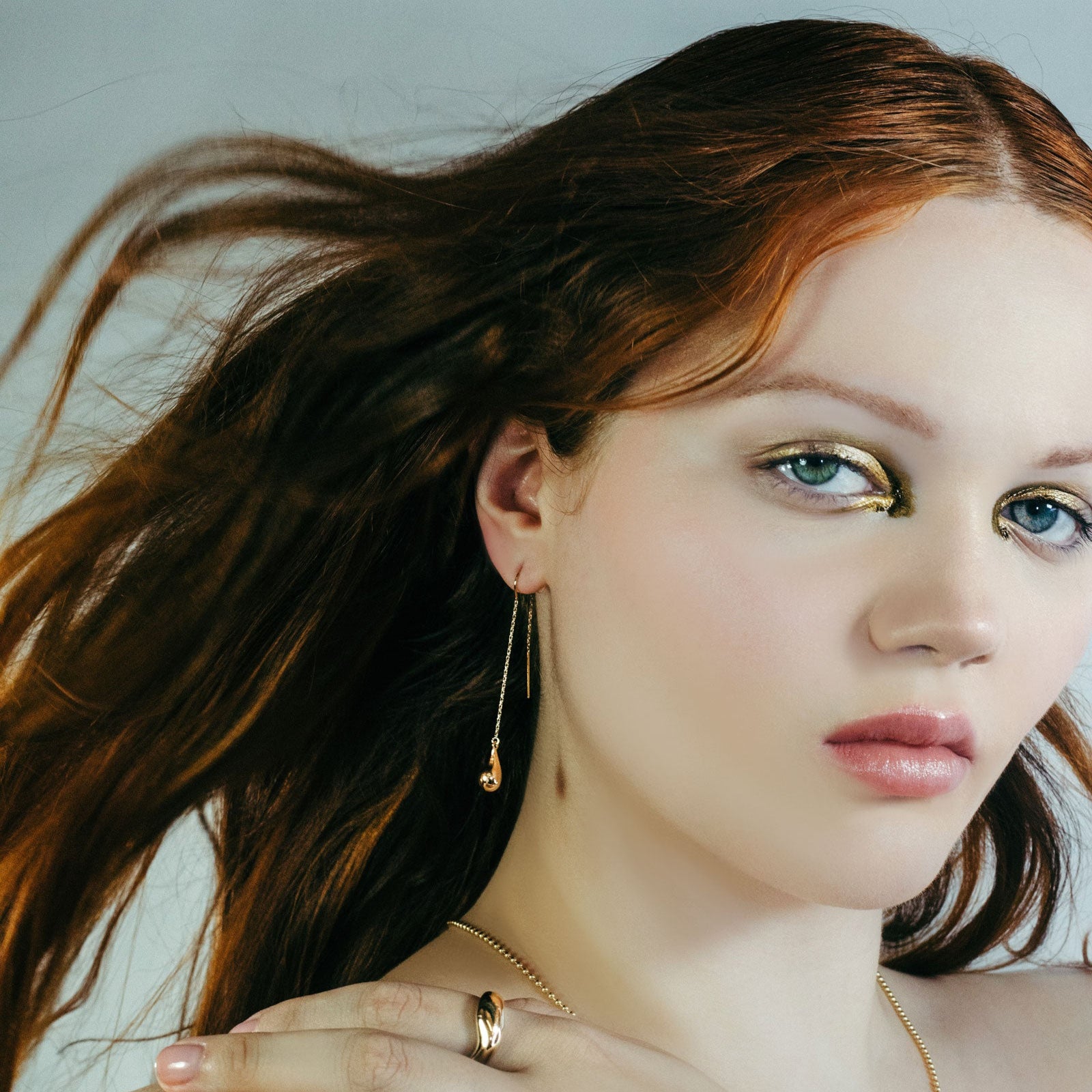 Flame haired model with molten threader earrings and molten ring, with molten gold eye shadow.