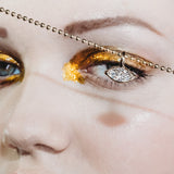 molten solitaire charm with marquise diamond over a models eye with molten gold eye shadow.