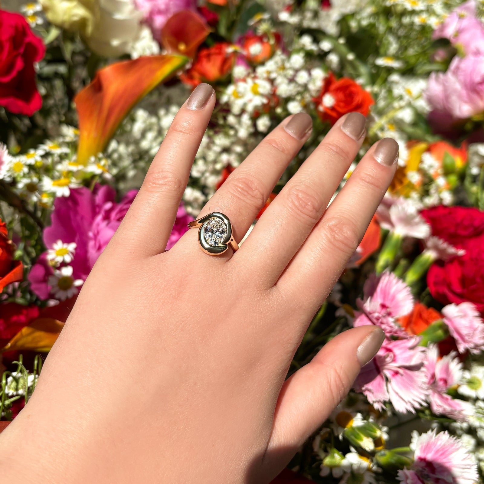 Molten knot ring with diamond on the hand over an expanse of colorful flowers.
