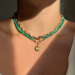 Yellow gold chain with green opal beaded necklace and round charm set with a light green peridot stone layered on neck.