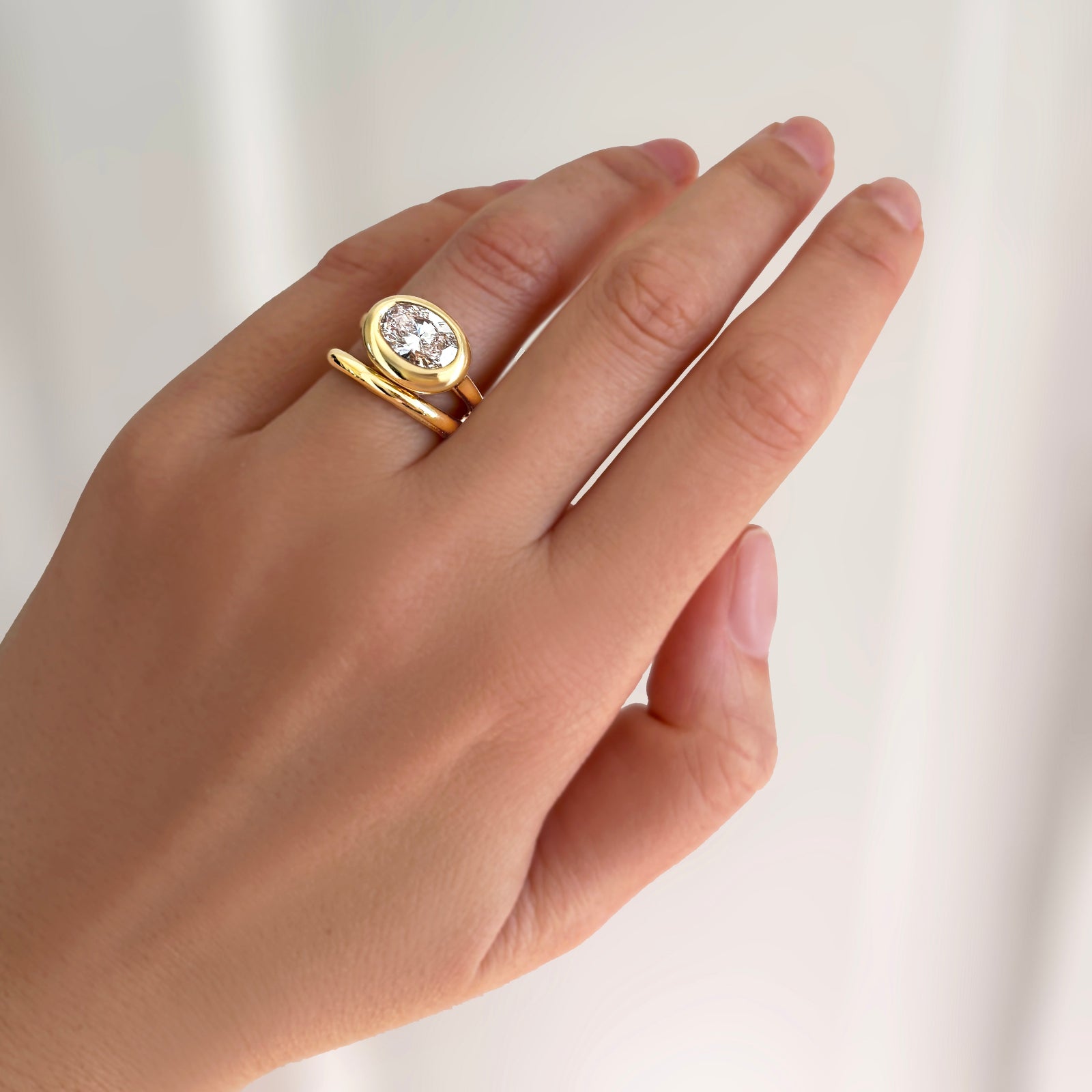 AMANDA PEARL 14k recycled yellow gold Molten solitaire ring with oval diamond with 14k recycled yellow gold molten band on a model's hand.