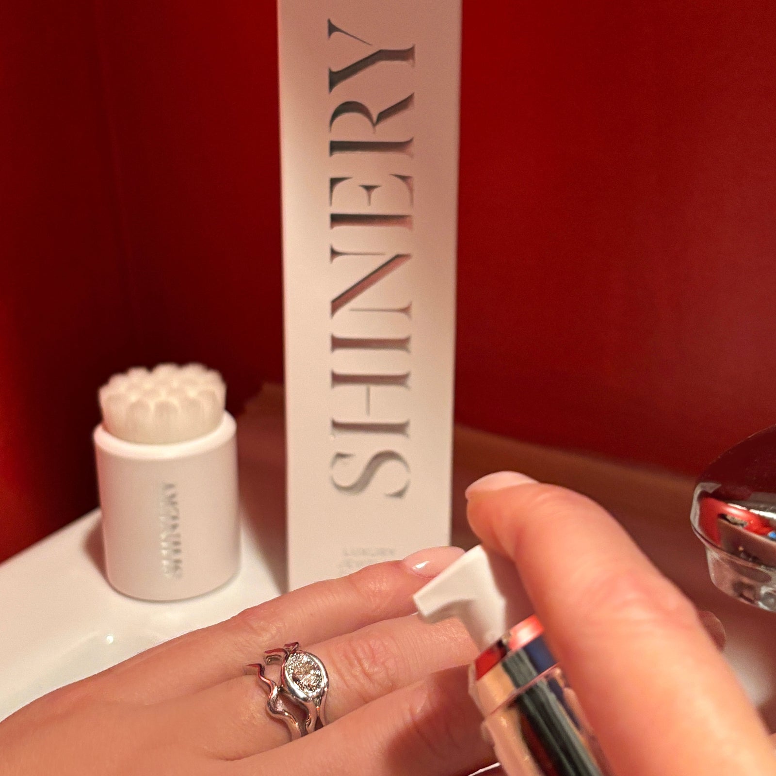 A model with a large diamond ring in the act of using Shinery Jewelry wash in a red bathroom. She is wearing the AMANDA PEARL ripple ring with diamond in 14K white gold.