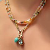 Natural multi faceted opal necklace layered with mermaid disco opal necklace with a charm lock and amazonite drop charm and blue topaz molten knot charm hanging from it.