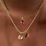 Omega chain with molten knot charm with round rose cut ruby layered with bead chain with citrine solitaire charm, and folded heart charm on the neck.