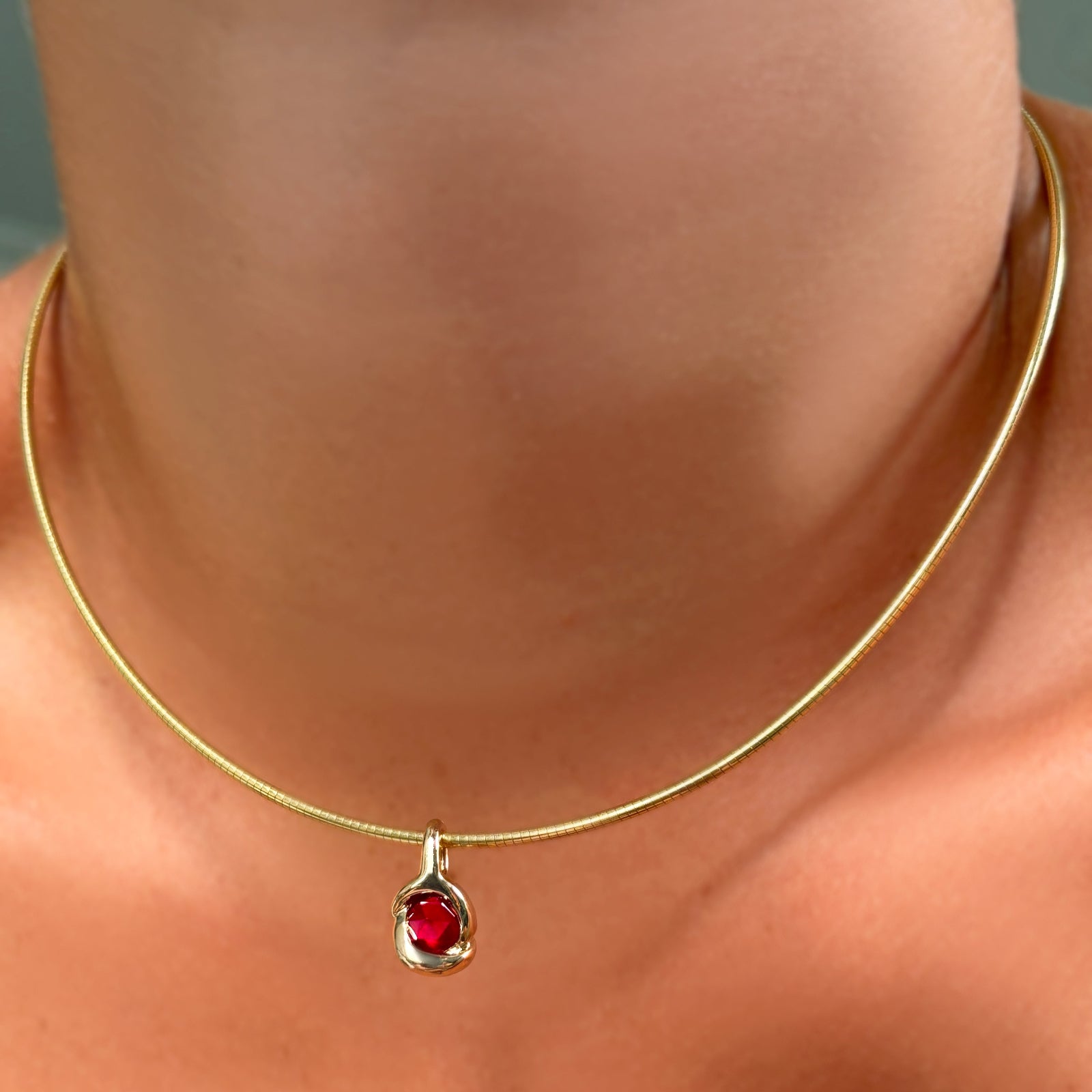 Omega chain with molten knot charm with round rose cut ruby on the neck.