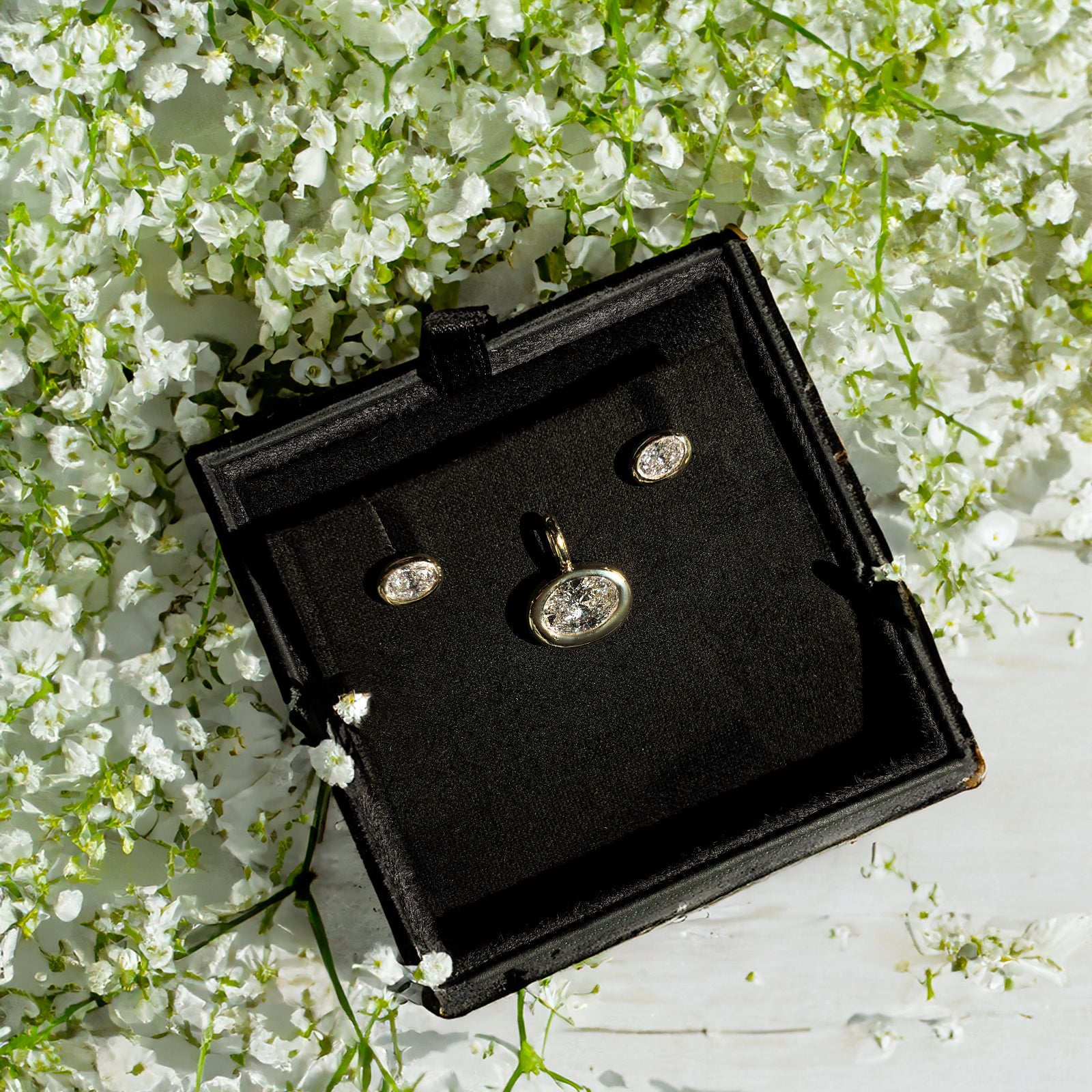 molten solitaire studs and charms in a gift box surrounded by small white flowers.