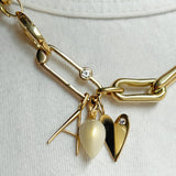 14K Gold Folded Heart Charm with white diamond styled on neck with multiple charms, hanging from chain and from a paperclip charm lock with diamond.