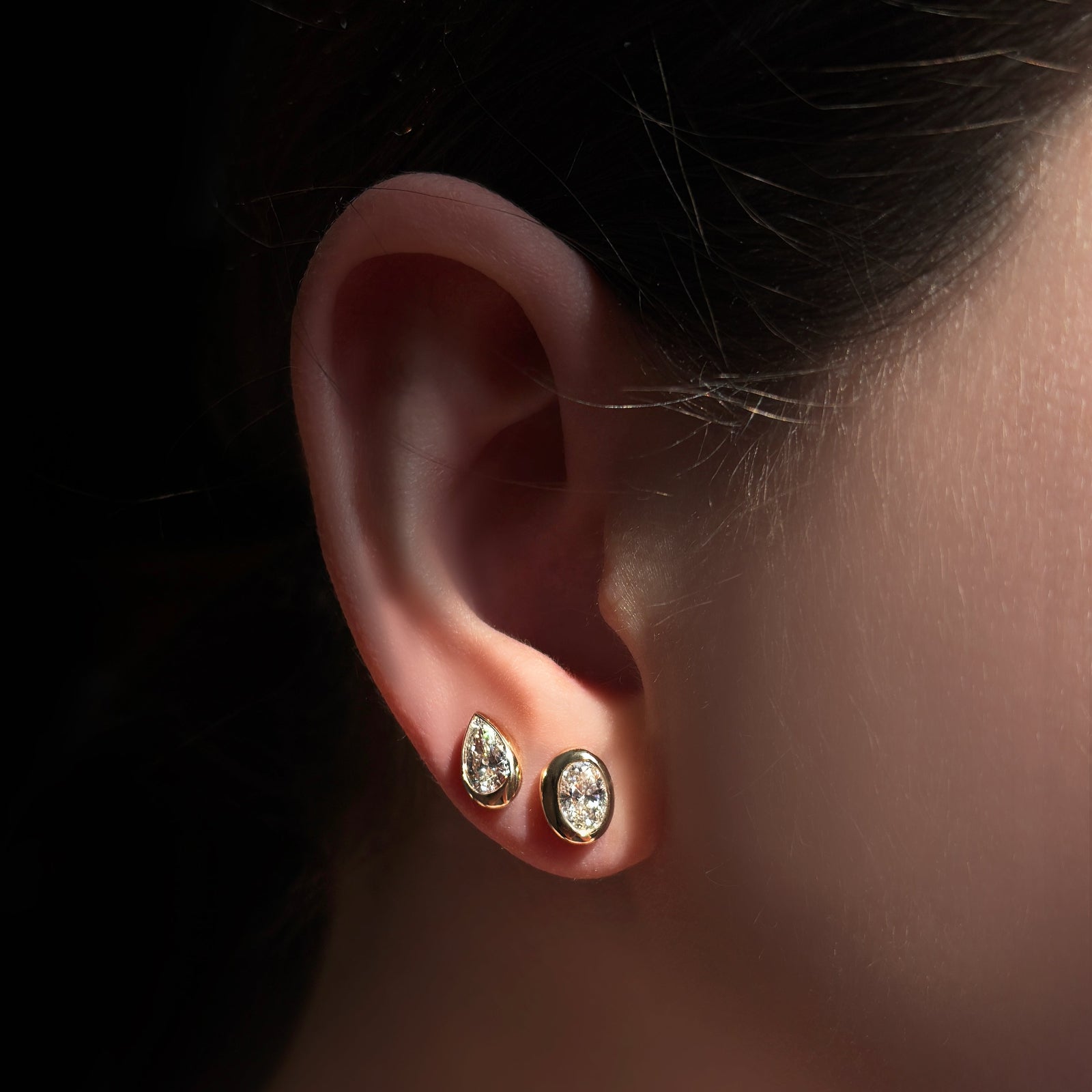 pear and oval molten solitaire studs set in yellow gold on the ear.