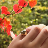 14K recycled Yellow Gold skull pinky ring styled on a hand, with fall leaves in the distance