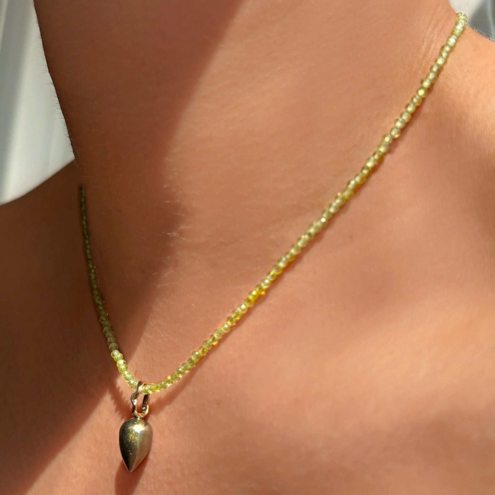 Pyrite acorn drop charm. Styled on a neck hanging from a beaded Peridot slim gemstone necklace. 