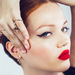 A model gazes into the camera, with her arm framing her face to show off her 14k recycled yellow gold Quill Bypass Rings, set with ethical lab grown diamonds.