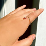 A 14K recycled yellow gold Quill Bypass Ring with bezel set round Ruby on a model's reaching hand.