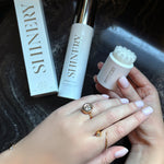 A model with a large quill bezel diamond ring in the act of using Shinery Jewelry wash with a marble background. She is holding the Shinery brush as though about to polish her ring.