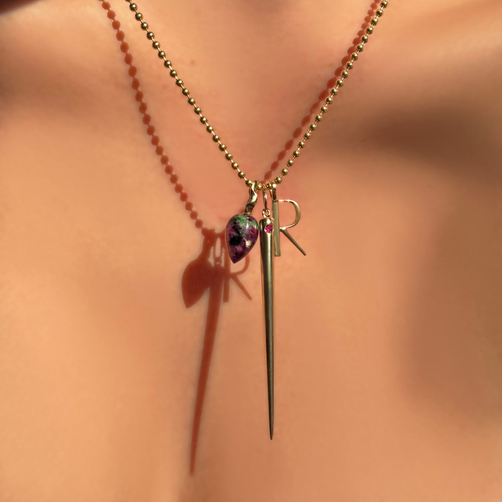 2mm bead chain with ruby zoisite drop charm, quill spike charm with ruby, and letter "R" charm in yellow gold on a model's neck.