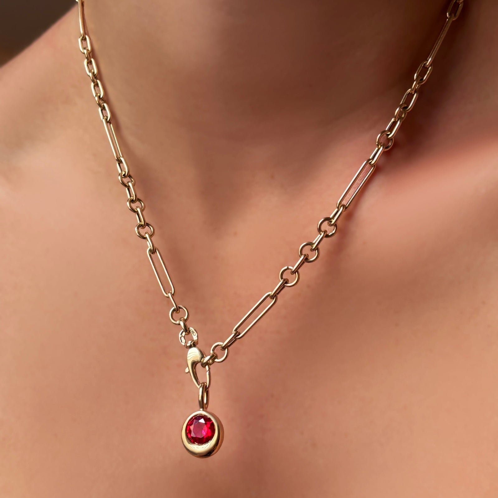 Round molten solitaire charm with ruby on a 6mm Irregular Cable Chain Necklace in 14k recycled yellow gold on a model's neck.