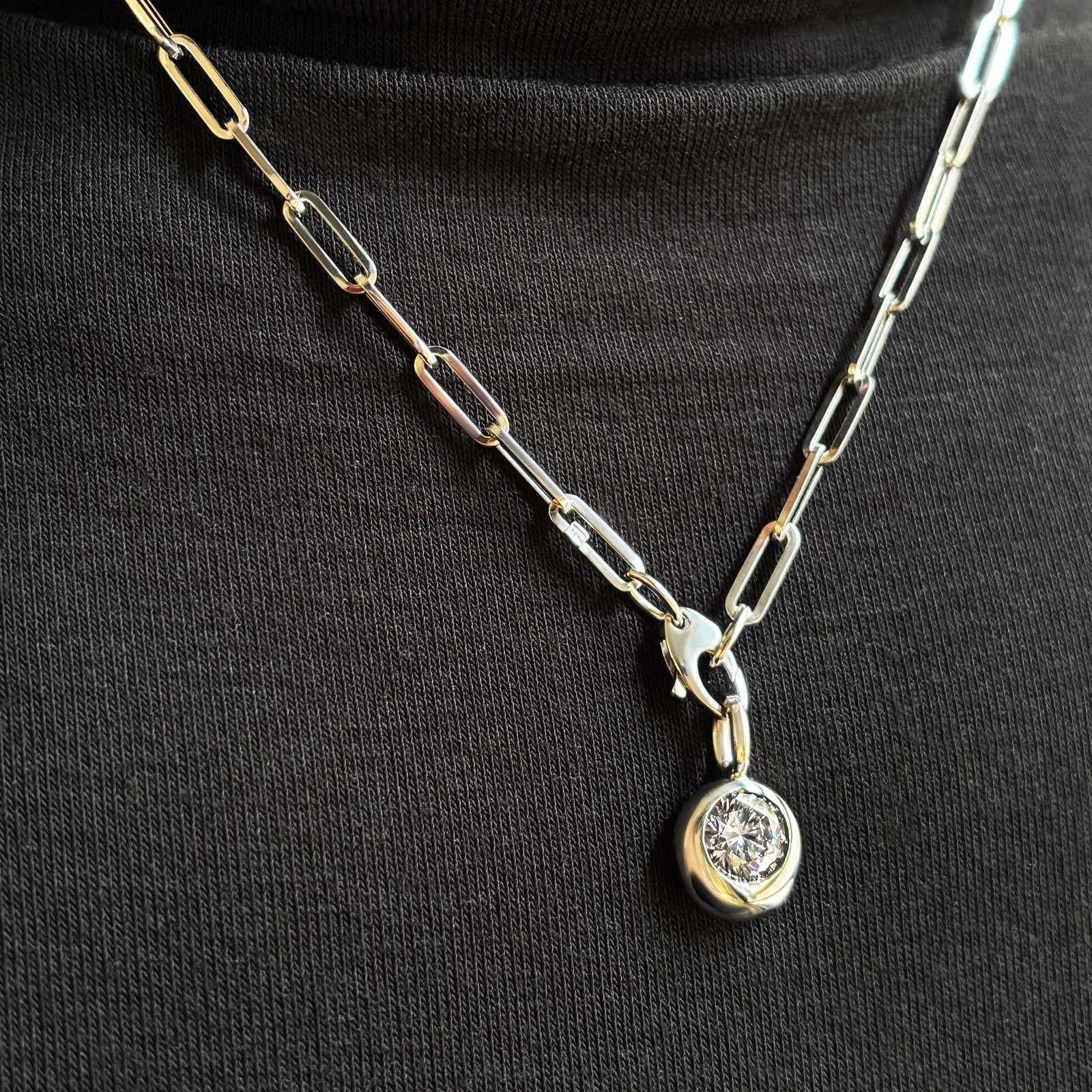 A round Molten solitaire charm in white gold, is styled with a chunky paper clip chain necklace also in white gold. In this ensemble, the charm is creatively hung from the clasp of the chain, to create an unexpected look.