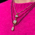 ruby, pink spinel, purple garnet slim gemstone necklaces with molten solitaire charms with diamonds worn over a bright pink sweater.