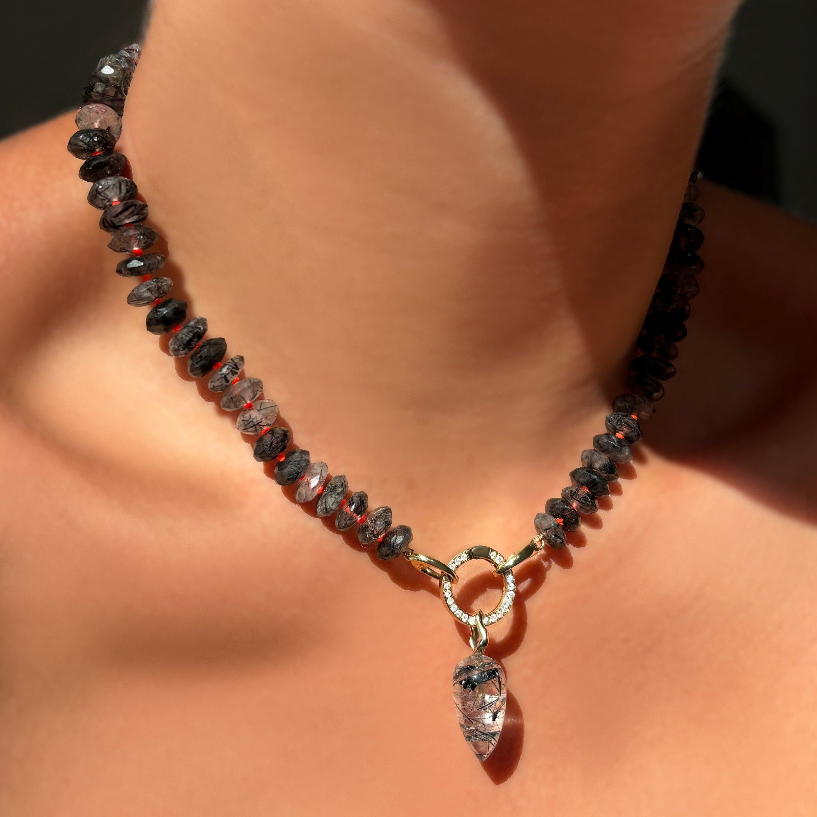 A model wears a rutilated quartz necklace, fastened with a round 14K yellow gold diamond pavé charm lock, and securing a quartz drop charm.