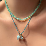 Sea glass green faceted opal necklace, layered with an apatite slim gemstone necklace with an aquamarine drop charm and molten knot charm with blue topaz hanging from it, on the body.