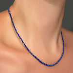 Slim gemstone necklace made of faceted 2mm lapis beads on a model's neck.