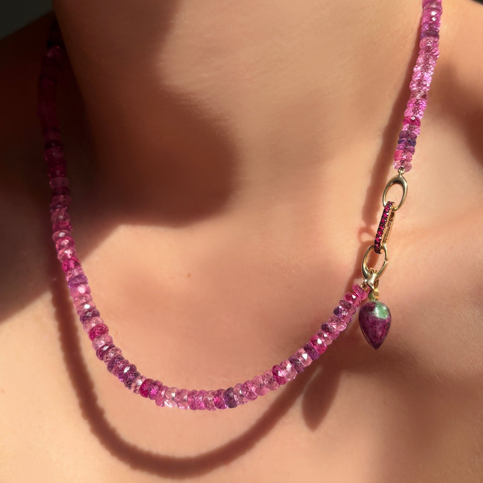 Fuchsia faceted sapphire necklace with ruby charm lock, and ruby zoisite drop charm with yellow gold ripple bale on a model's neck