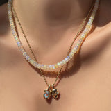 Supermoon faceted opal necklace layered with a gold bead chain, molten knot charm with blue topaz, and molten skull charm hanging on the neck.