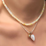 Slim gemstone necklace in moonstone with mini molten drop charm and rainbow moonstone drop charm with recycled 14k yellow gold bale, layered under a supermoon faceted opal necklace, hanging from a model's neck.