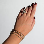 A model wears a tibet chain bracelet, a drop link bracelet, and a bead chain bracelet, as well as a molten knot ring with an ethical lab grown diamond. These pieces are made from 14K yellow gold. 