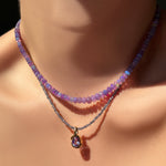 Purple beaded Necklace with a 14K recycled yellow gold amethyst molten knot charm pendant on a model's neck against a dark background.